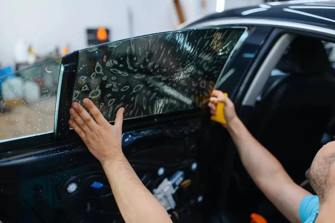 Installer wet-mounting dark window film onto the front door glass of a black car and pressing the slip solution out with a squeegee