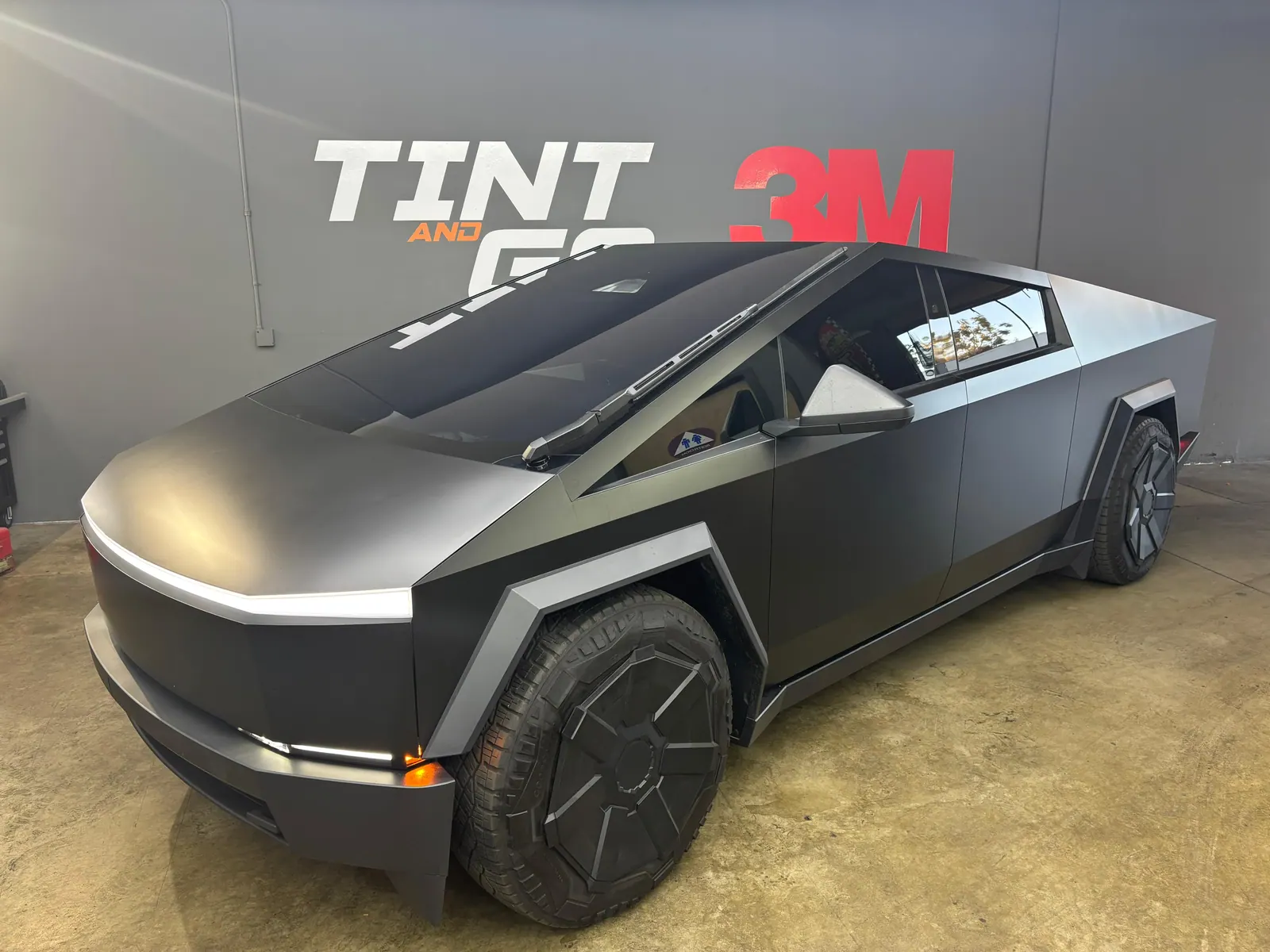 Tesla Cybertruck finished in satin black film, parked under the Tint and Go Pro and 3M wall graphic