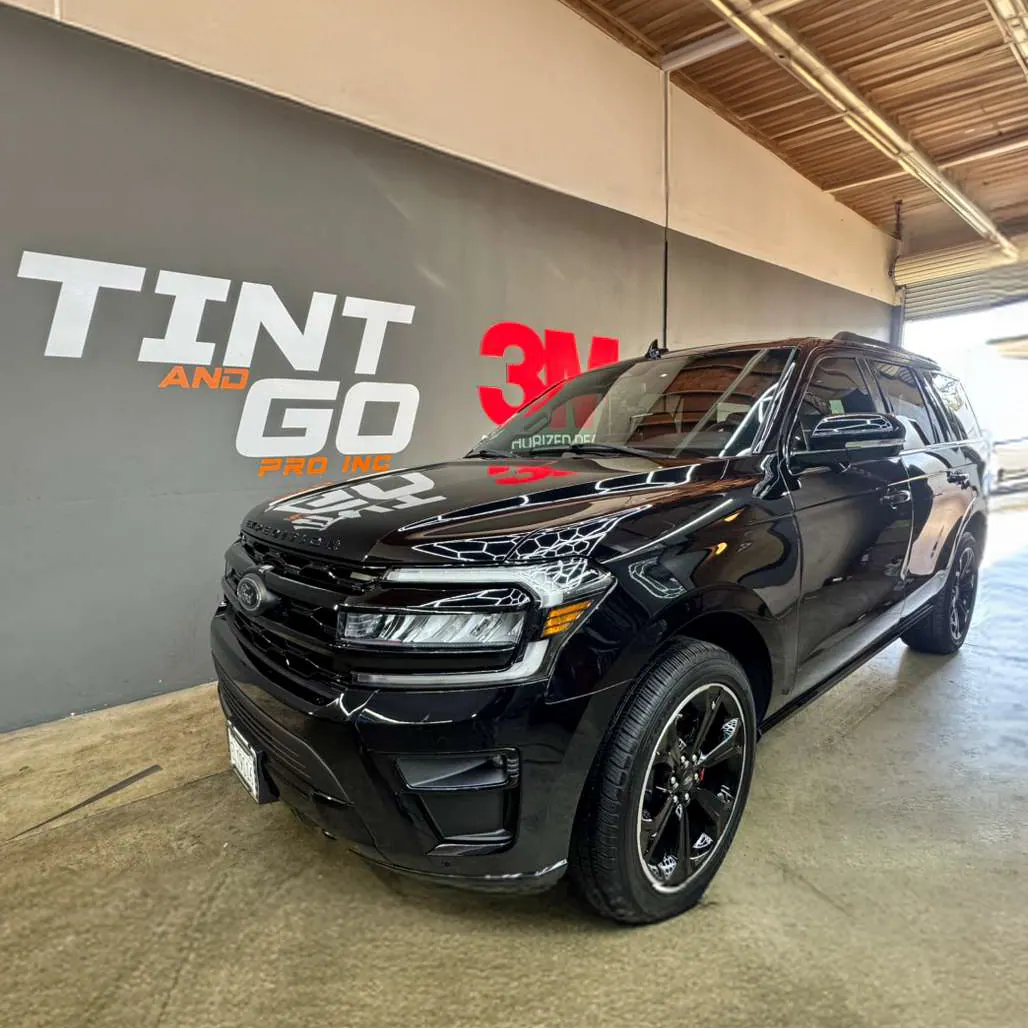 Black full-size SUV with tinted glass parked in the Tint & Go Pro bay beneath the shop's wall graphic