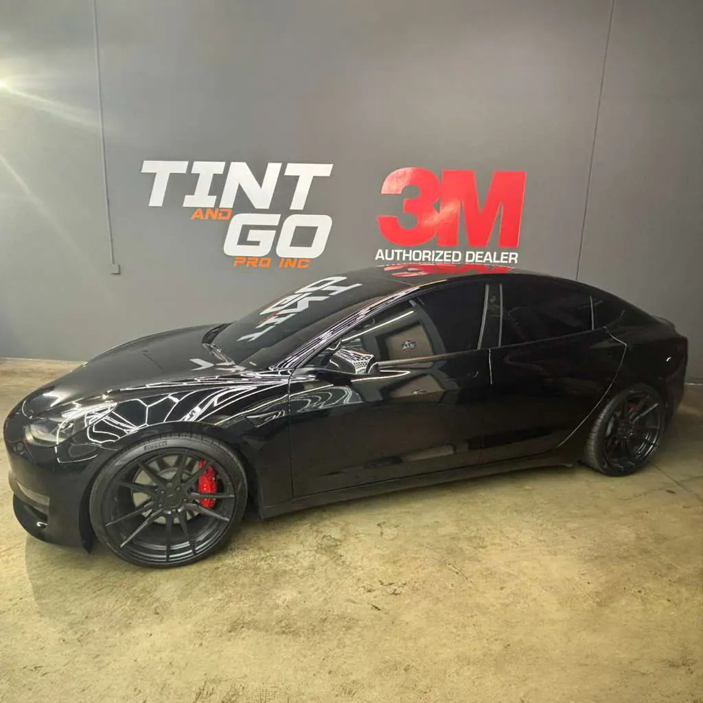 Black Tesla Model 3 with red brake calipers and tinted windows inside the Tint & Go Pro shop