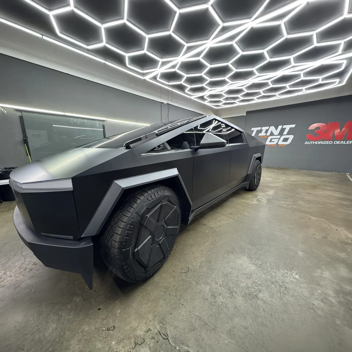 Matte black wrapped Tesla Cybertruck under the studio's hexagonal ceiling lights