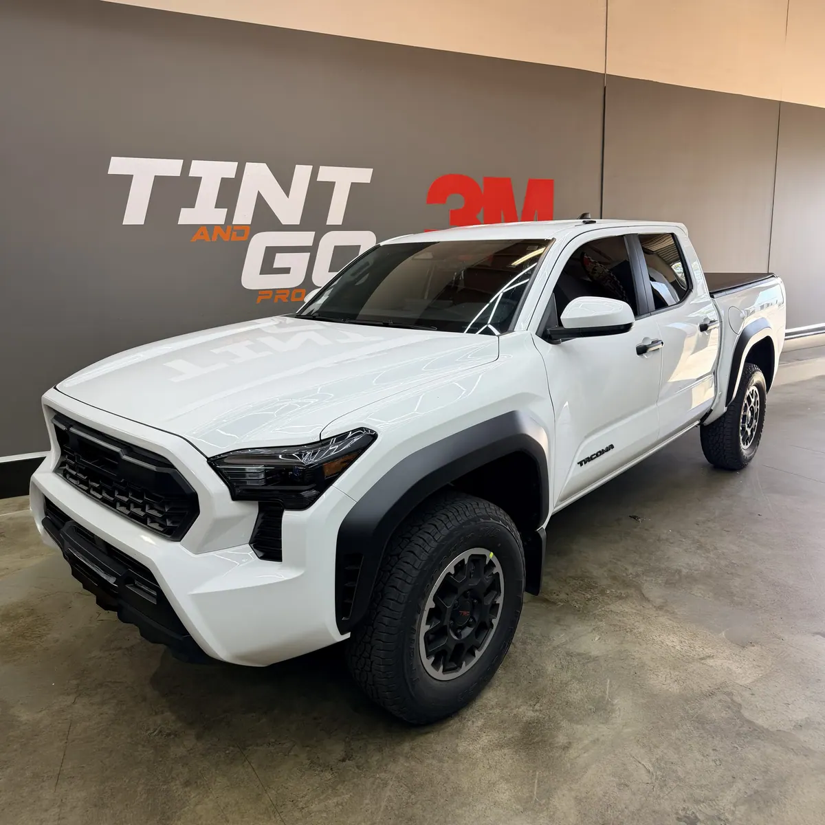 White Toyota Tacoma with tinted windows parked under the shop's wall graphic