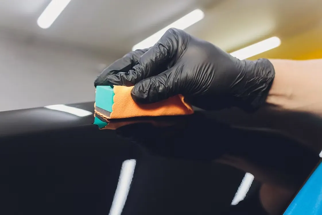 Gloved hand drawing ceramic coating across a black body panel with a foam applicator block