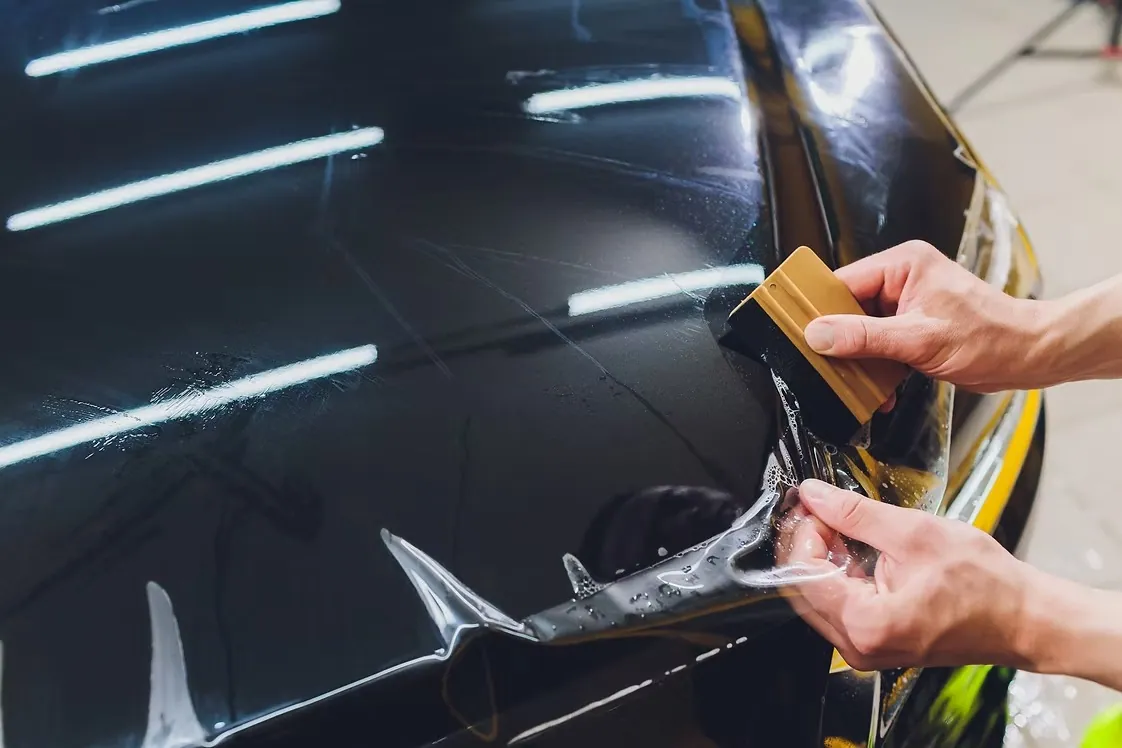 Installer squeegeeing a sheet of clear paint protection film down onto the glossy black front fender of a car