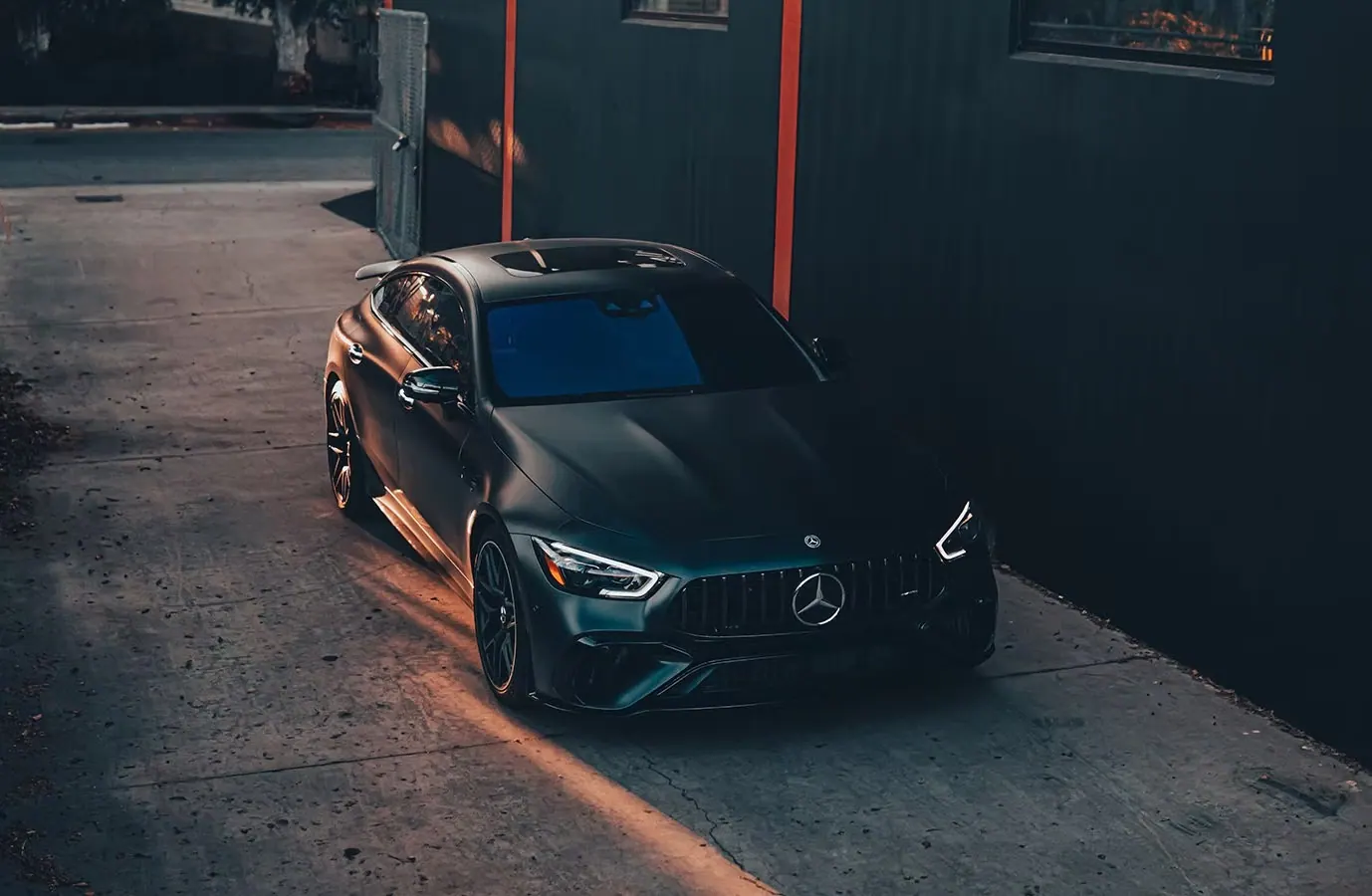 Matte black coupe with tinted windows beside the entrance to an automotive shop